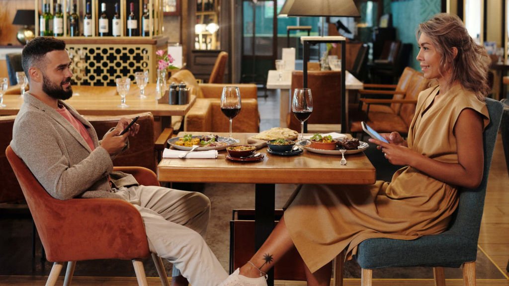 a man and a woman sitting at a table with food and drinks