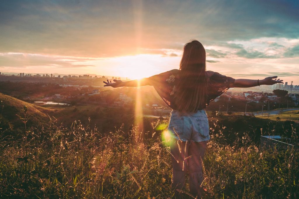 a person standing in a field with their arms out towards the sun