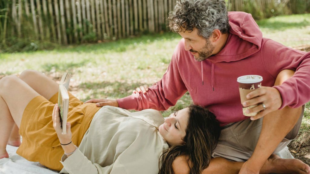 a man and woman sitting on the ground holding cups of coffee