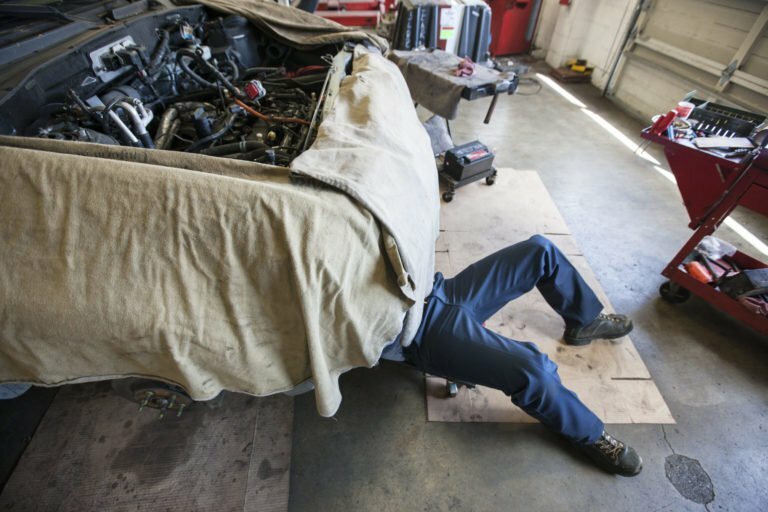 Mechanic lays on a trolley under a car in an auto repair shop